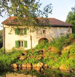 Visionssuche in den Vogesen, Bild zeigt Ferienhaus im Sonnenlicht mit Teich im Vordergrund